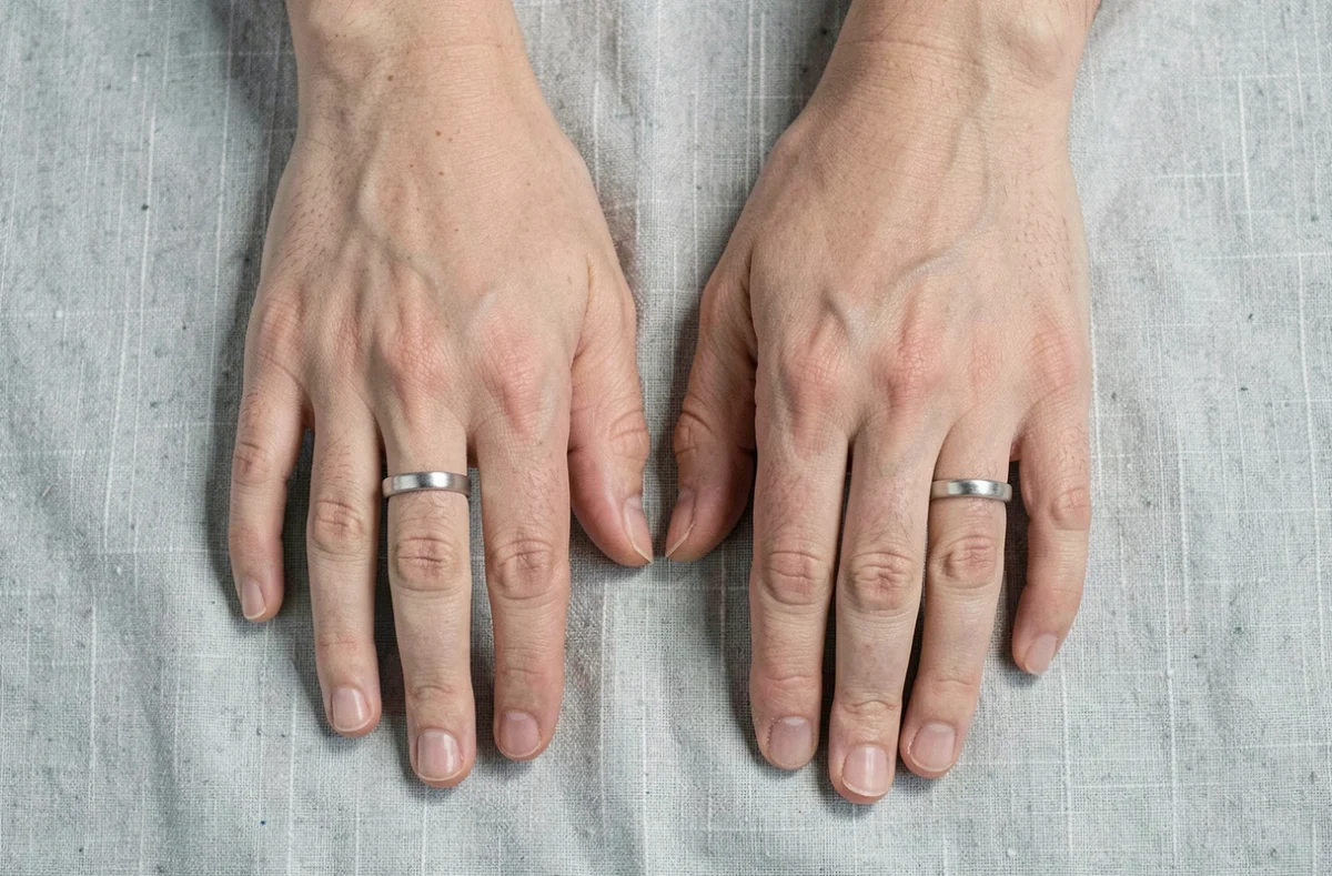 Comparaison de deux morphologies de mains portant des bagues en argent de tailles différentes sur un textile gris clair