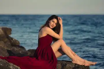 woman in red dress sitting on rock near sea during daytime