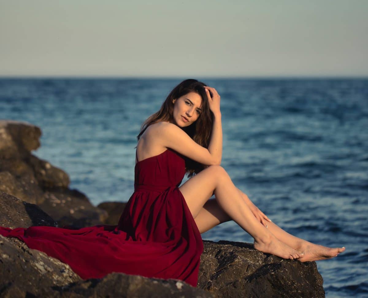 woman in red dress sitting on rock near sea during daytime