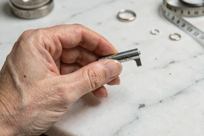 Femme mesurant la taille de son doigt avec un mandrin de mesure de bagues en métal sur un plan de travail en marbre blanc
